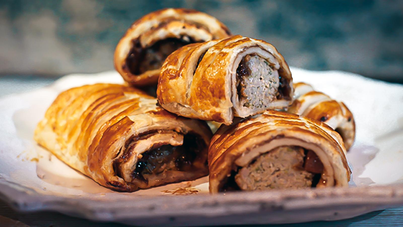 Golden flaky sausage roll fresh from the oven on a wooden board